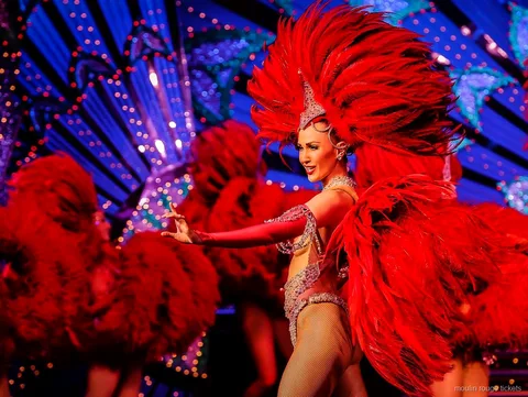 Dançarina com um grande leque de penas vermelhas diante de um cenário azul iluminado, bilhetes Moulin Rouge