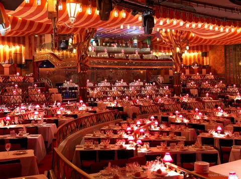 Bilhetes Moulin Rouge: o salão do cabaré com teto listrado de vermelho, mesas em níveis e abajures rosa
