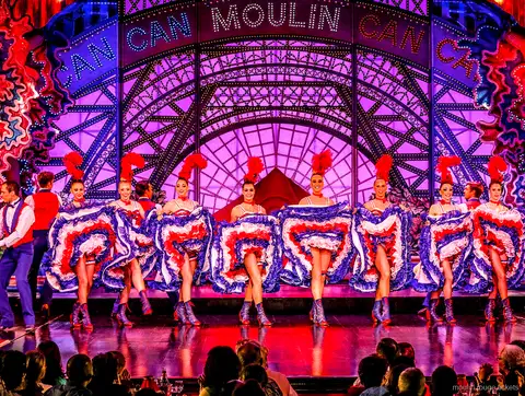 Bailarina de cancán en un salto abierto con falda azul de volantes y su pareja, cena espectáculo Moulin Rouge