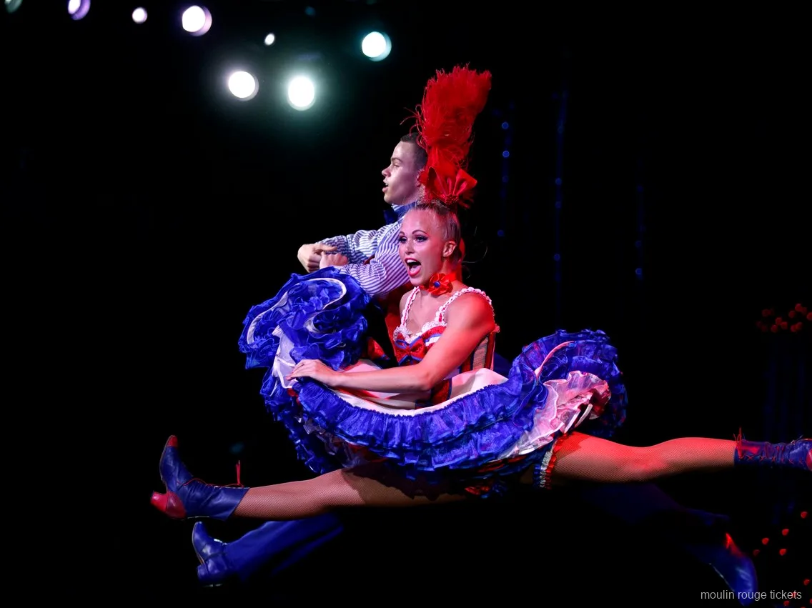 Público frente a la fila de French Cancan bajo el rótulo luminoso Moulin, cena espectáculo Moulin Rouge