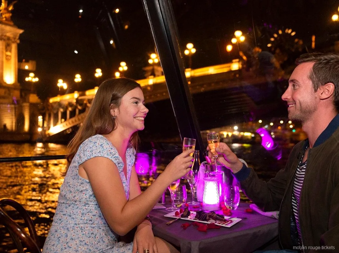 Pareja brindando con champán en una cena crucero nocturna por el Sena, antes del show con entradas Moulin Rouge