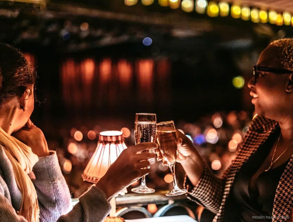Deux spectatrices trinquent au champagne près d'une lampe de table, billets Moulin Rouge du soir