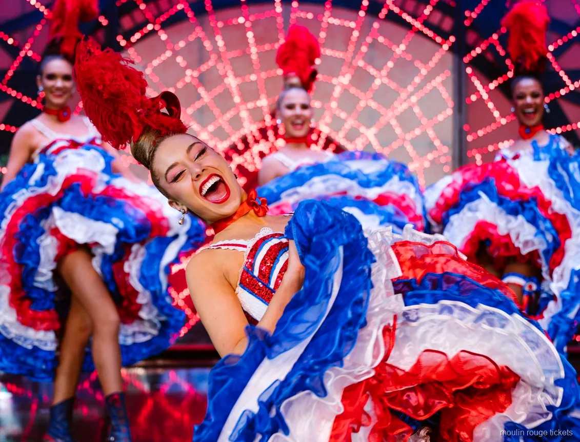 Dançarina de cancã sorrindo com saia de babados vermelha, branca e azul, jantar e show Moulin Rouge