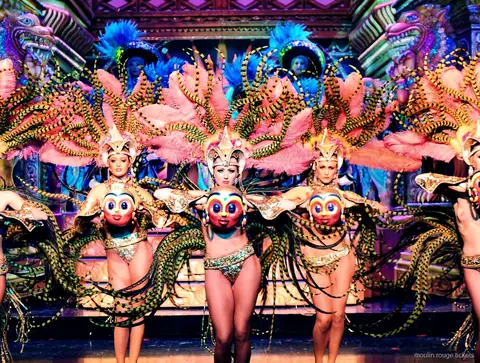 Dansare med rosa randiga fjädervingar och gyllene masker framför en utsmyckad kuliss, Moulin Rouge dinner show