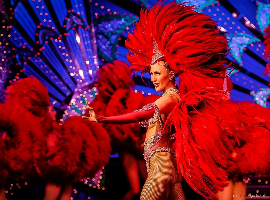 Dansare med en stor röd fjädersolfjäder framför en blått upplyst kuliss, Moulin Rouge showbiljetter