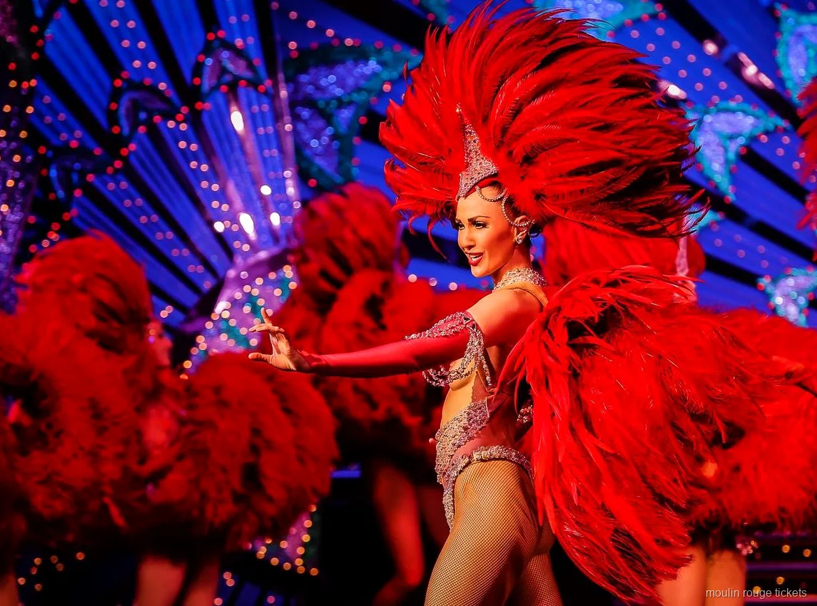 青く光る舞台装置の前で大きな赤い羽根の扇を広げて踊るダンサーと後ろに並ぶ踊り子たち、ムーランルージュ チケットで観るショー