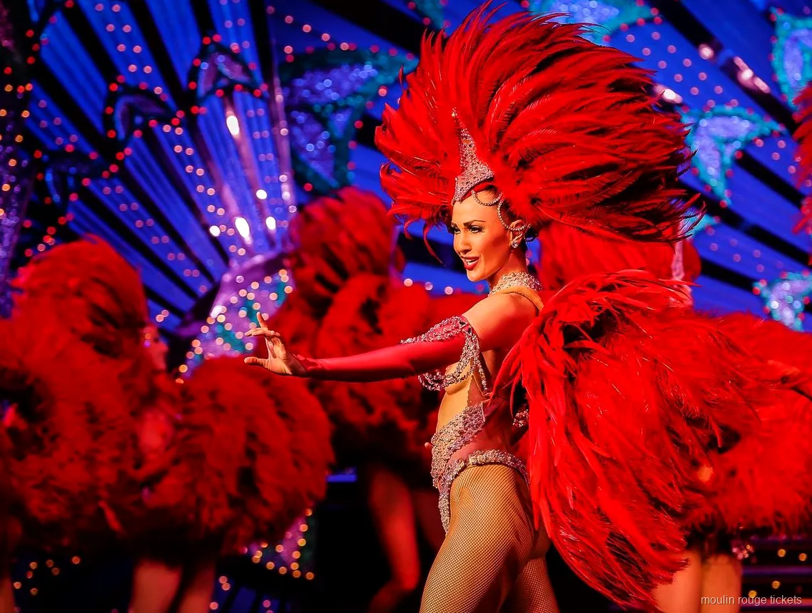 Dancer with a giant red feather fan in front of a blue lit set, seen with Moulin Rouge show tickets