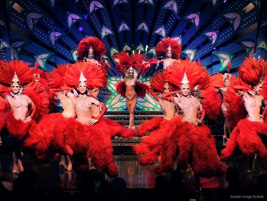 Kırmızı tüylü kostümler ve parıltılı başlıklarla sahnedeki dansçılar, Moulin Rouge biletleri ile izlenen revü