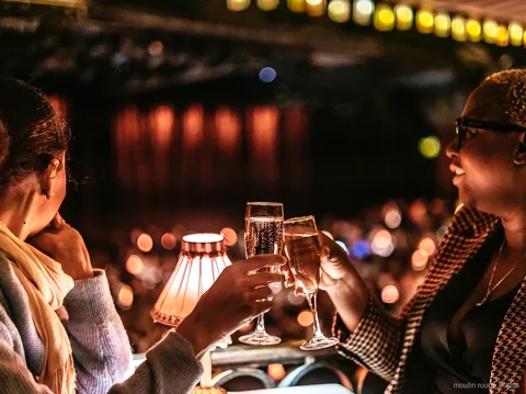 Twee gasten proosten met champagne aan een tafel met lampje, Moulin Rouge tickets voor de avondshow