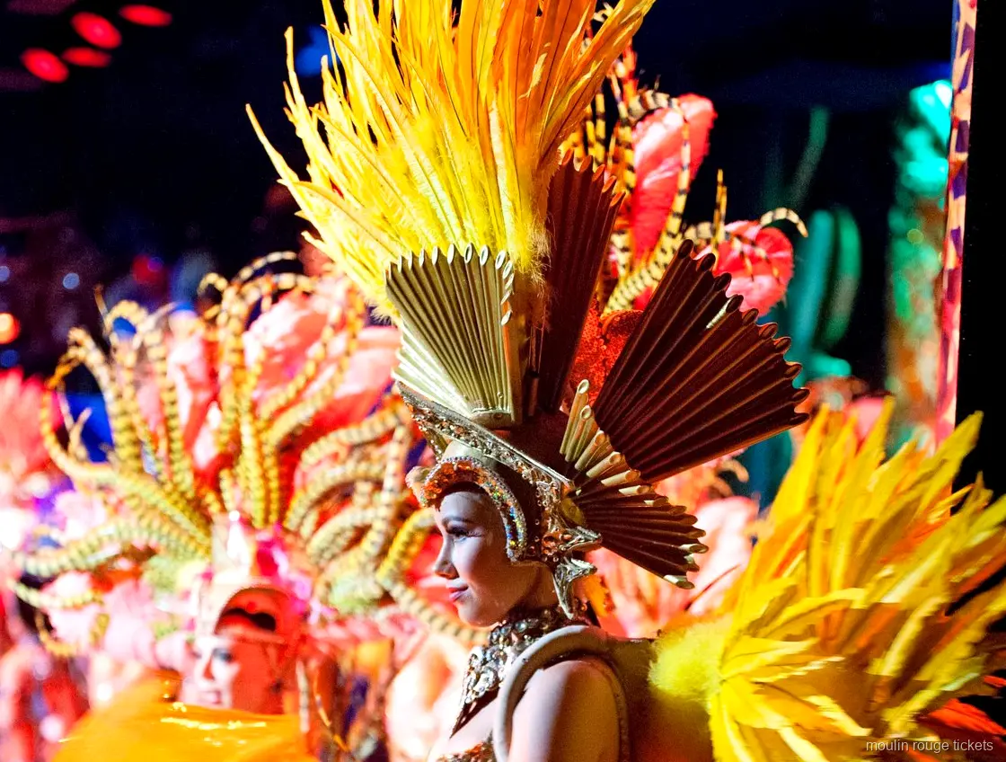 Moulin Rouge biljetter: dansare med guldfärgad fjäderhuvudbonad och solfjäderskrona på scenen