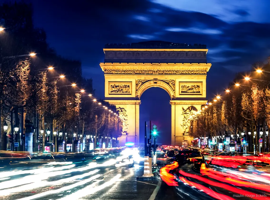 Arco di Trionfo illuminato di notte in fondo agli Champs Élysées con scie luminose, tappa prima dei biglietti Moulin Rouge